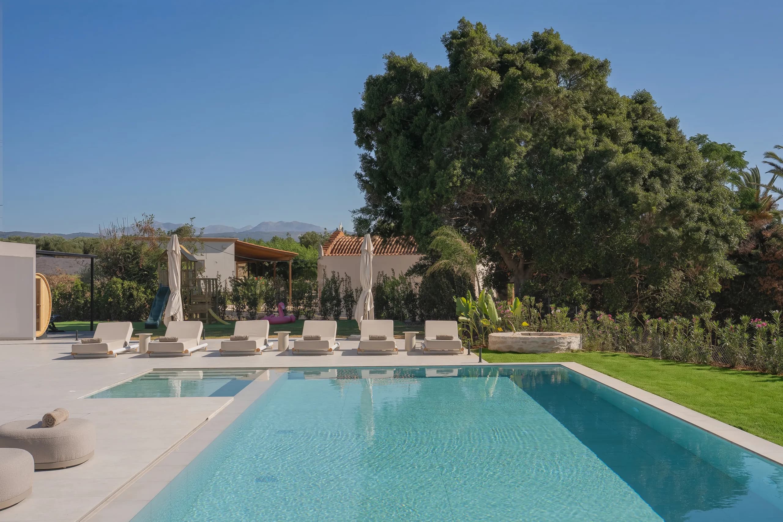 Left Crete's private pool, loungers, garden and mature trees in daylight