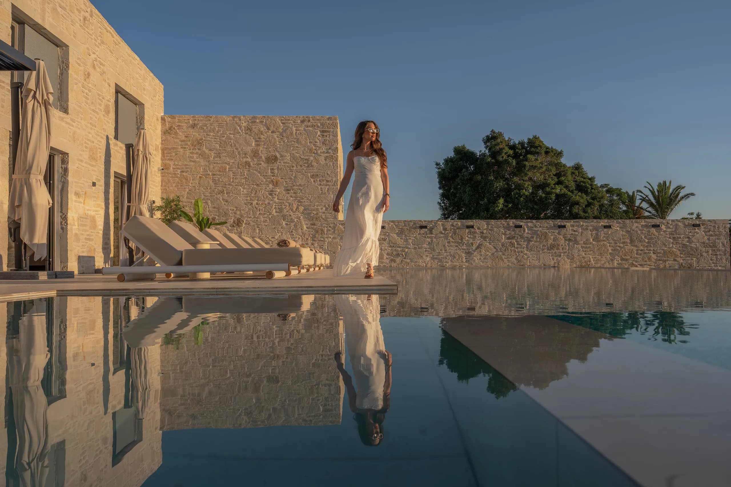 A guest walking beside Right Crete's pool and stone facade in evening light