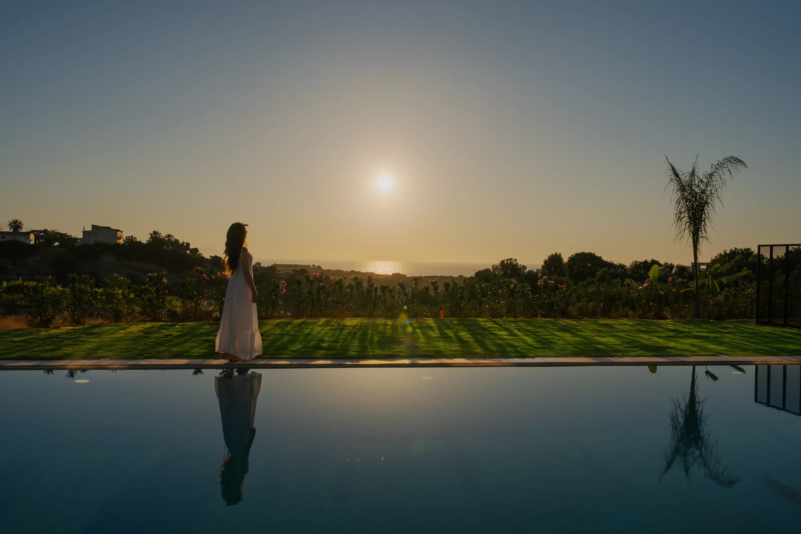 A guest beside Left Crete's pool looking toward the Cretan Sea at sunset