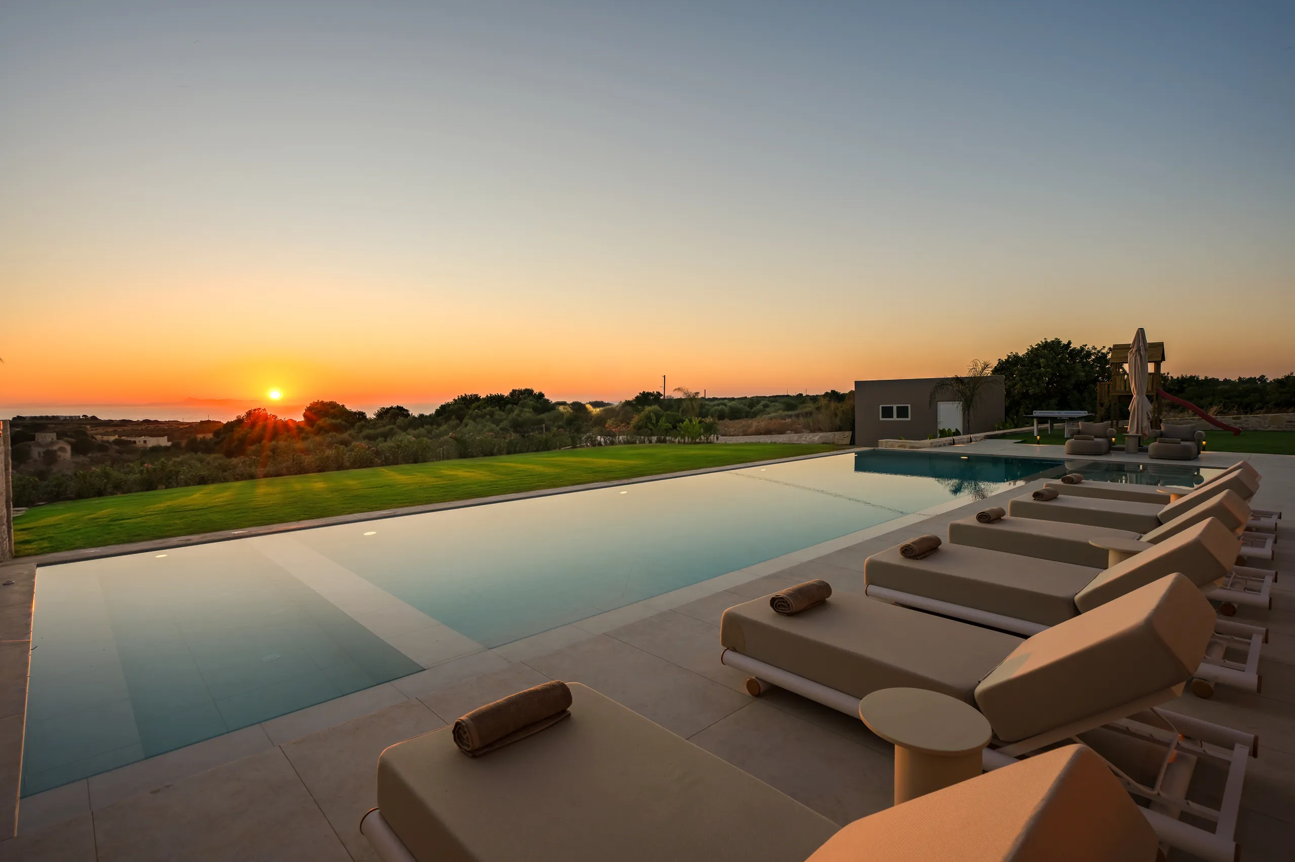 Right Crete's pool and prepared loungers facing the sunset over the Cretan Sea